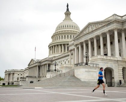 A man wearing a mask depicting American flags jogs past the U.S. Capitol Building, Tuesday, April 28, 2020, in Washington. The U.S. House of Representatives has canceled plans to return next week, a reversal after announcing it a day earlier. (AP Photo/Andrew Harnik)