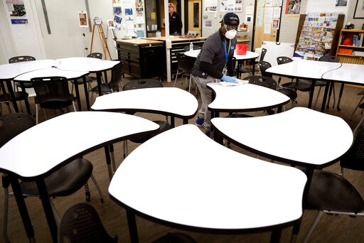 Des Moines Public School employee Sam Teah sanitizes a desk in a classroom at Central Campus high school, Thursday, March 19, 2020, in Des Moines, Iowa. All Des Moines public schools are closed in response to the coronavirus outbreak. (AP Photo/Charlie Neibergall)