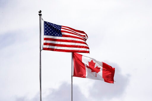 In this photo taken Sunday, May 17, 2020, U.S. and Canadian flags fly atop the Peace Arch at Peace Arch Historical State Park on the border with Canada, where people can walk freely between the two countries at an otherwise closed border, in Blaine, Wash. Canada and the U.S. have agreed to extend their agreement to keep the border closed to non-essential travel to June 21 during the coronavirus pandemic. The restrictions were announced on March 18, were extended in April and now extended by another 30 days. (AP Photo/Elaine Thompson)