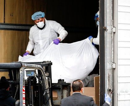 A body wrapped in plastic is loaded onto a refrigerated container truck used as a temporary morgue by medical workers wearing personal protective equipment due to COVID-19 concerns, Tuesday, March 31, 2020, at Brooklyn Hospital Center in Brooklyn borough of New York. The new coronavirus causes mild or moderate symptoms for most people, but for some, especially older adults and people with existing health problems, it can cause more severe illness or death. (AP Photo/John Minchillo)