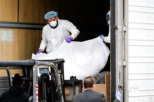 A body wrapped in plastic is loaded onto a refrigerated container truck used as a temporary morgue by medical workers wearing personal protective equipment due to COVID-19 concerns, Tuesday, March 31, 2020, at Brooklyn Hospital Center in Brooklyn borough of New York. The new coronavirus causes mild or moderate symptoms for most people, but for some, especially older adults and people with existing health problems, it can cause more severe illness or death. (AP Photo/John Minchillo)