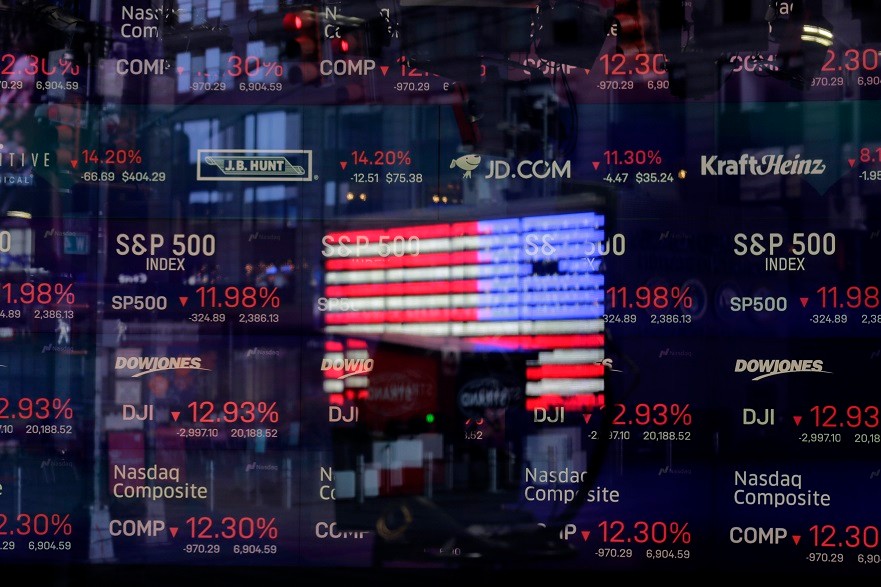 A United States flag is reflected in the window of the Nasdaq studio, which displays indices and stocks down, in Times Square, New York, Monday, March 16, 2020. (AP Photo/Seth Wenig)