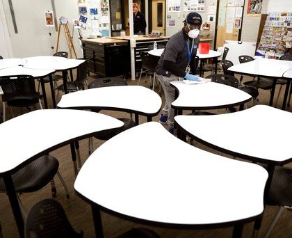 Des Moines Public School employee Sam Teah sanitizes a desk in a classroom at Central Campus high school, Thursday, March 19, 2020, in Des Moines, Iowa. All Des Moines public schools are closed in response to the coronavirus outbreak. (AP Photo/Charlie Neibergall)