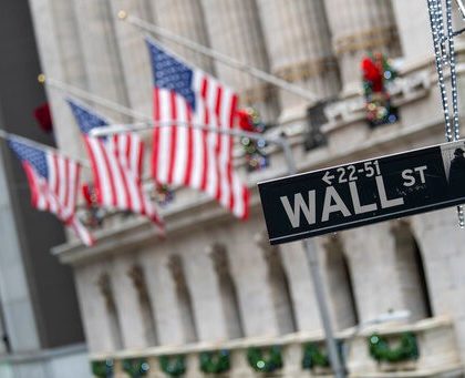 The Wall St. street sign is framed by American flags flying outside the New York Stock Exchange, Friday, Jan. 3, 2020, in New York. Stocks fell broadly on Wall Street in midday trading Friday and oil prices surged after U.S. forces in Iraq killed a top Iranian general. (AP Photo/Mary Altaffer)