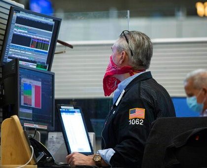In this photo provided by the New York Stock Exchange, trader Eric Schumacher wears a bandana face mask as he works on the partially reopened trading floor, Tuesday, May 26, 2020, in New York. Stocks surged on Wall Street in afternoon trading Tuesday, driving the S&P 500 to its highest level in nearly three months, as hopes for economic recovery overshadow worries about the coronavirus pandemic. (Colin Zimmer/New York Stock Exchange via AP)